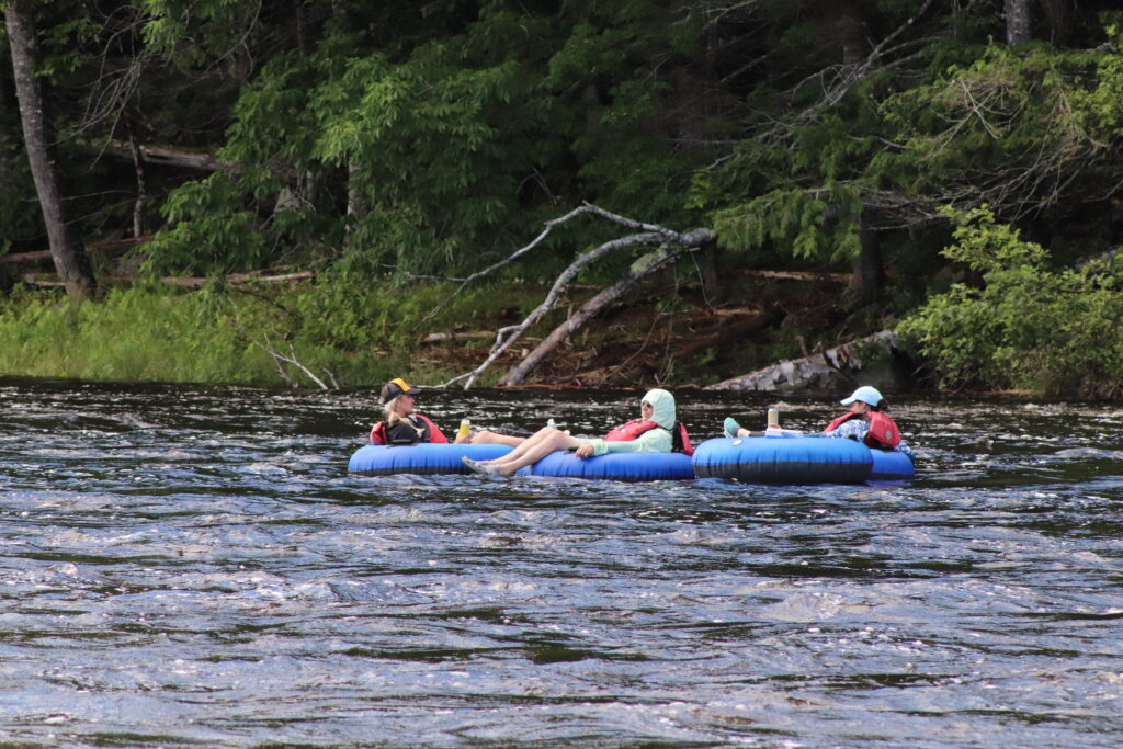 Three people sitting in blue tubes floating on the Kennebec River